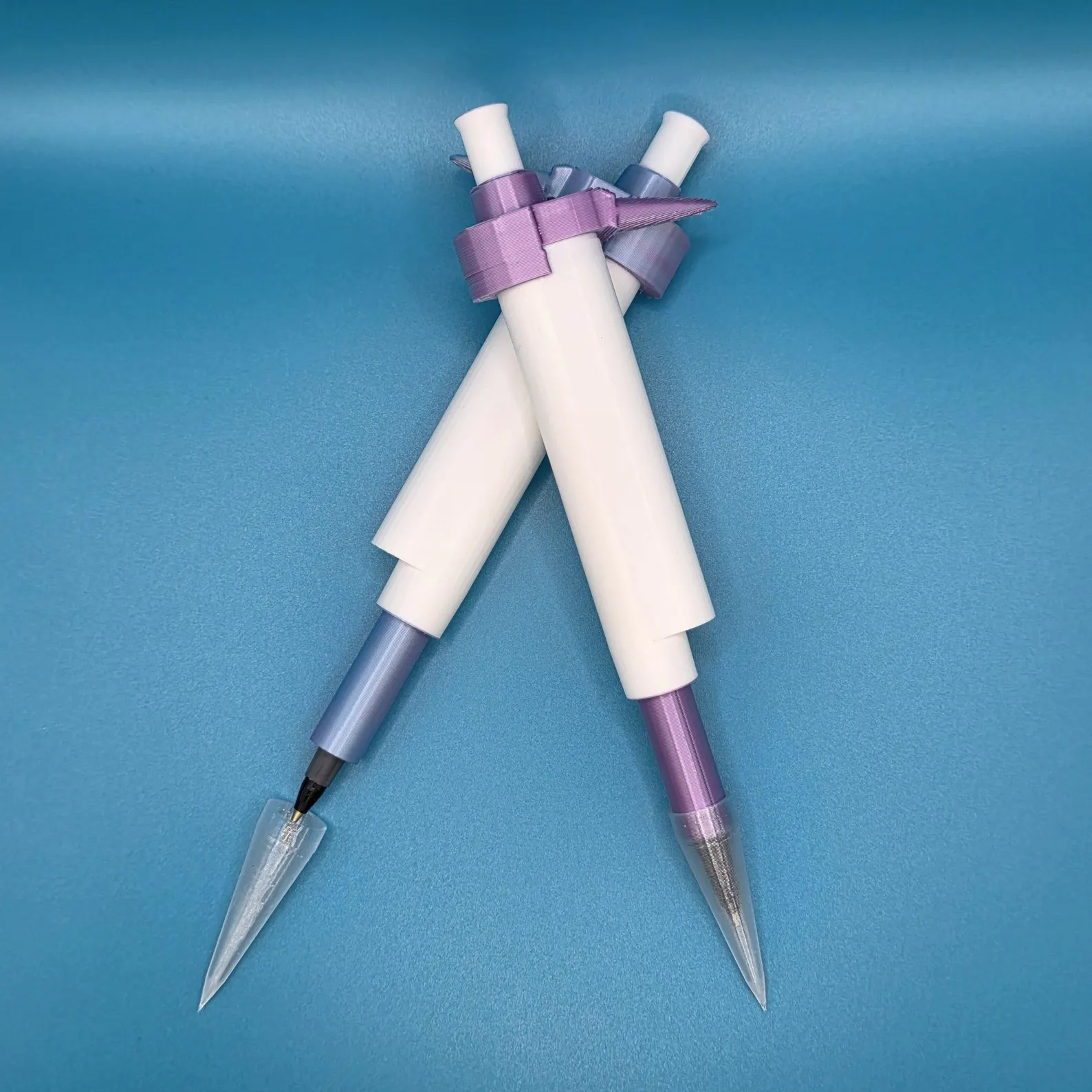 A pair of custom micropipette-shaped pens, 3D-printed in white with purple and blue-grey accents and ribbon detailing